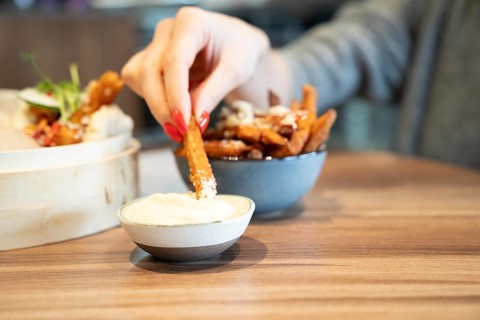 Hand dipping sweet potato fry into sauce on wooden table