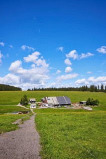 Path to a small farmstead in a landscape with meadows and forest under a blue sky with cumulus
