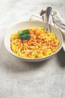 Risotto with shrimp, in a bowl, on a textured surface, with a side dish of fresh coriander,