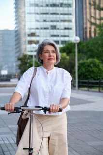 A mature woman in a white shirt enjoys a leisurely scooter ride through an urban setting,