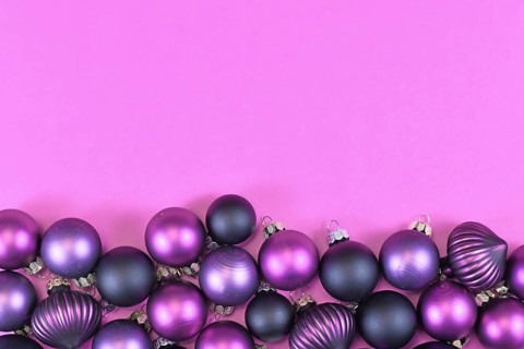 Seasonal dark purple and pink Christmas tree bauble ornaments at bottom of pink background with