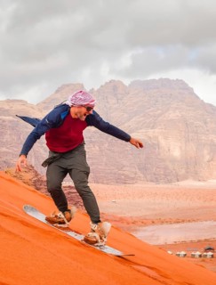 Man successfully sandboarding down steep red dune in Wadi rum showing skill balance confidence