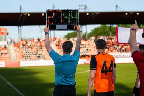 Assistant referee displaying substitution board during a soccer match with stadium crowd in the