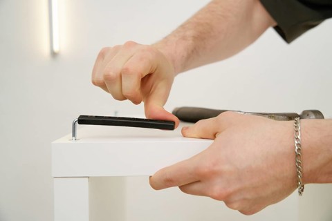 Cropped unrecognizable view of a man's hands using a hex key to assemble new white furniture. The