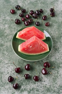 Top view of juicy watermelon slices on a vibrant green plate, surrounded by scattered cherries on a
