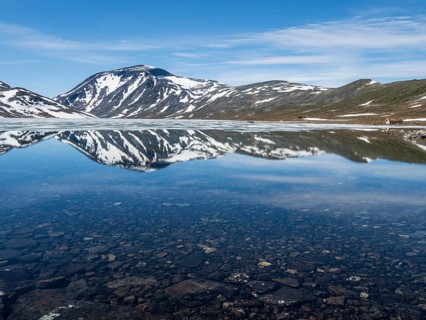 Melting ice on mountain lake Bessvatn, reflections on calm surface, Jotunheimen National Park,
