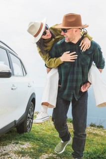 Close up happy couple enjoys holiday time together piggyback check mirror by white SUV during