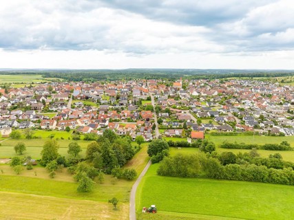 Aerial view of a wide village with red roofs and green meadows, embedded in the landscape under a