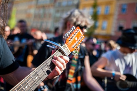 Close-up shot of a musician playing a 12-string acoustic guitar with a capo during an outdoor