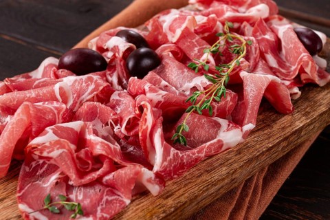 Freshly cut dried meat, served with olives and herbs, on a wooden chopping board, no people