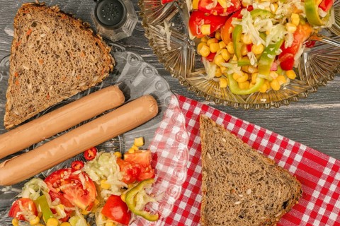 Sausages with bread and vegetable salad on a picnic table