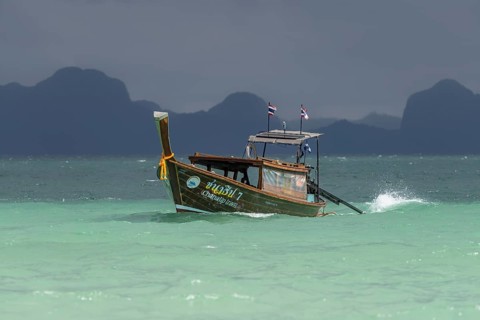 Longtail boat travelling fast to the beach, behind it an approaching thunderstorm, Koh Ngai Island,