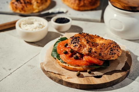 A delicious bagel topped with fresh salmon, capers, and greens, served on a rustic wooden board
