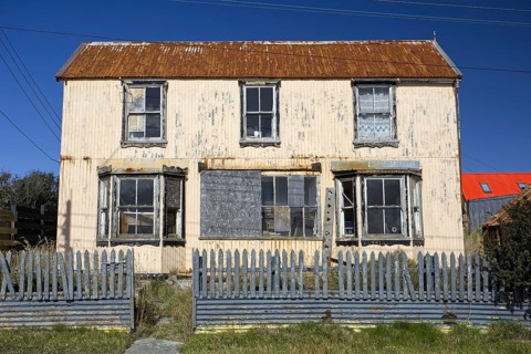 Dilapidated two-storey house with rusty corrugated iron roof, broken and barricaded windows,