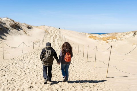 A couple of backpackers hand in hand walk along the hilly sand dunes on the Curonian Spit,