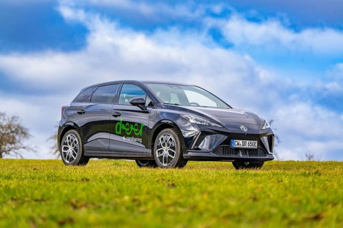 Black car with green lettering in a meadow under a cloudy sky, e-car sharing, Deer Mobility, MG4,