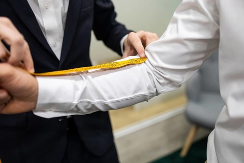 A close up of a tailor measuring the arm of a client with a yellow measuring tape in a suit store.