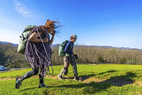 Two women climbers are walking on a meadow carrying climbing ropes and other gear, enjoying the