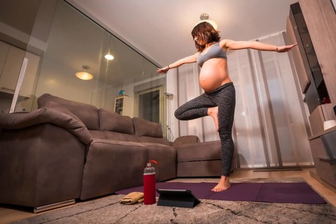 Young pregnant caucasian woman doing pilates exercise at home in the room. Online exercises in