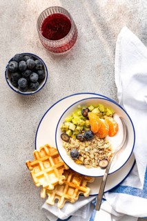 A top view of a healthy breakfast spread featuring yogurt with granola, fresh kiwi, orange slices,