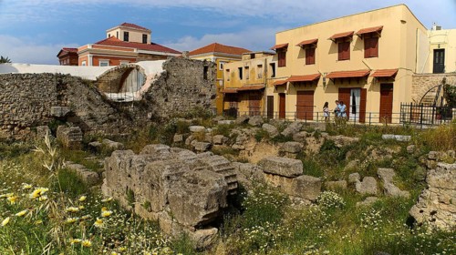 Ruins next to yellow houses and wild flowers, shining in the sun, Rhodes Old Town, Rhodes,