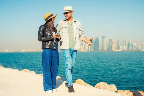 Doha Qatar tourist couple walking Corniche waterfront West Bay with skyline skyscrapers background