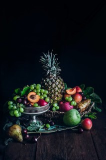 A lush arrangement of fresh tropical fruits including pineapple, apricots, grapes, and cherries,