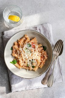 A bowl of cavatappi pasta garnished with cheese, fresh spinach leaves and spicy tomato sauce on a