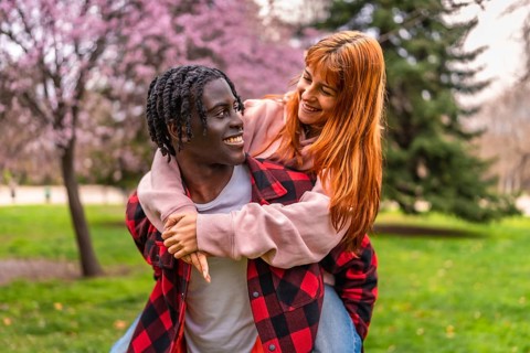 Interracial couple having fun in a park during springtime, the boyfriend is giving a piggyback to