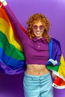 Studio portrait with purple background of a woman with curly hair and sunglasses waving lgbt