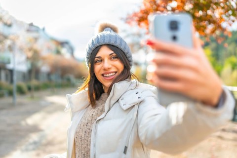 Confident woman smiling while taking selfie standing outdoors in a sunny winter day