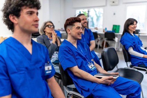 Young medical students and an experienced trainer sitting in a classroom, listening attentively
