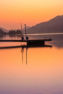 Footbridge at dusk, silhouettes of people on a quiet lake surrounded by mountains, Großer Alpsee,