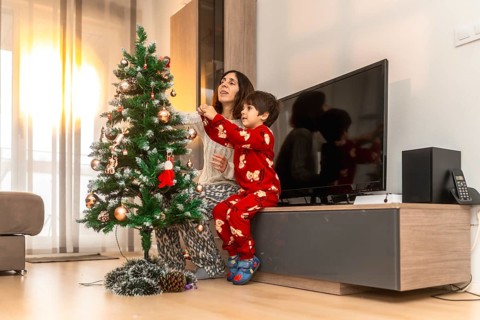 Mother and son dressed in pajamas happily decorating a christmas tree together with ornaments and
