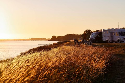 Coastline, grasses in the evening sun, tourists, motorhome parking, idyllic waterfront location,