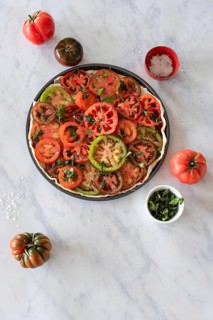 A vibrant salad featuring sliced heirloom tomatoes garnished with fresh herbs. Presented on a