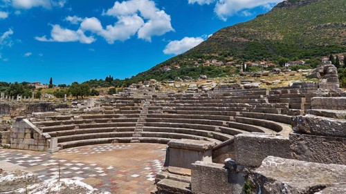 Ekklesiasterion, stone ancient amphitheatre against a mountain backdrop under cloud-covered sky,