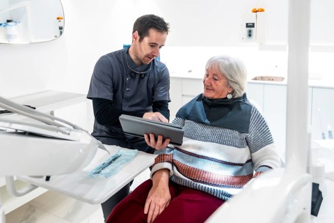 Dentist showing diagnosis and treatment plan on digital tablet to a senior woman patient during