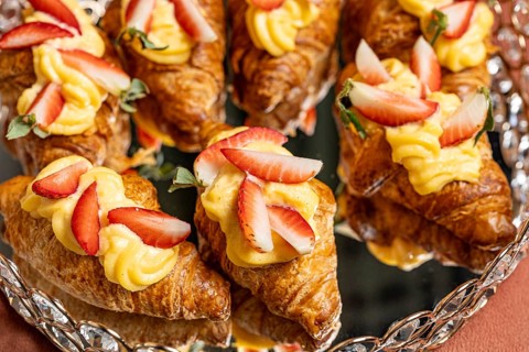 A batch of golden croissants adorned with creamy custard and fresh strawberry slices. Perfect for a