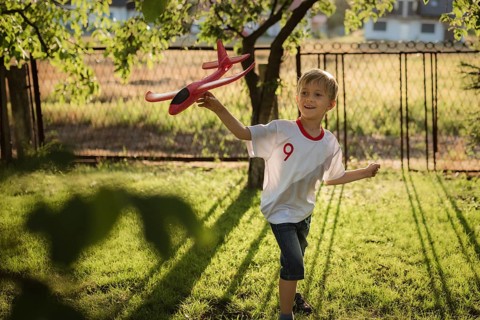 A boy in a T-shirt with the coat of arms of Poland plays with a plane in the garden