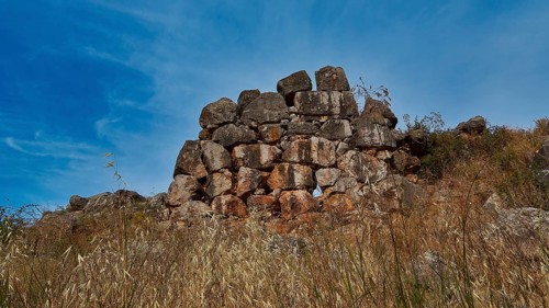 Ancient stone ruins on a grassy hill under blue sky, Tiryns, ancient city in Argolis, Mycenaean,