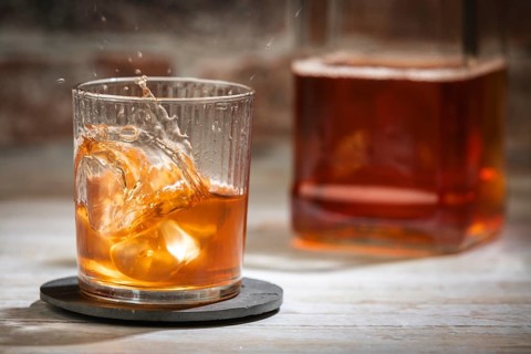A glass with sparkling whiskey, carafe in the background, bright surroundings