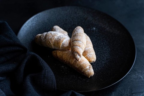 On a dark plate, homemade golden croissants with a light dusting of flour are arranged. The rustic