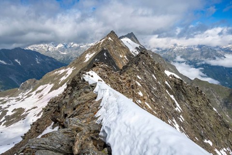 Snow-covered mountain ridge with view of surrounding peaks under a clear blue sky, summit of the