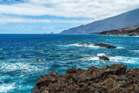 El hierro volcanic coastline featuring dark rocks along the shore, with turquoise atlantic ocean