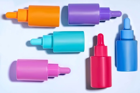 An overhead view of six colorful serum bottles in orange, purple, blue, and pink shades, neatly