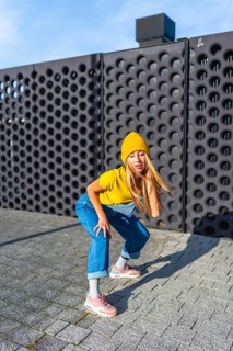 Young woman showcasing her urban dance moves in a dynamic pose, wearing a yellow beanie, t shirt,