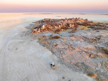 Rocky island with baobab trees in a dry salt pan, at sunset, off-road vehicle on the salt pan,