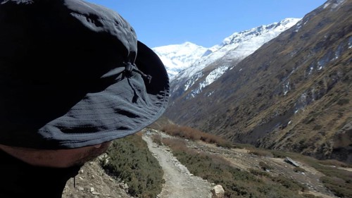 Person wearing hat looking at a majestic mountain landscape with snow-capped peaks, trekking at