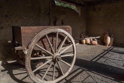 Old wooden cart and ceramic jugs on display inside an unenclosed building at the ancient ruins of